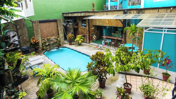 A courtyard with a swimming pool, potted plants, outdoor furniture, and a blue building in the background. - The Blue Suites & Spa (La Fortuna)