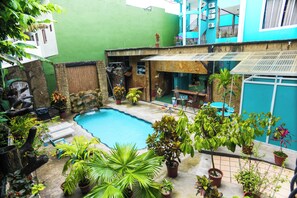 A courtyard with a swimming pool, potted plants, outdoor furniture, and a blue building in the background. - The Blue Suites & Spa (La Fortuna)