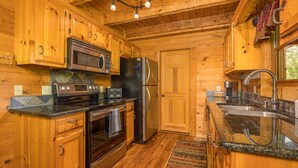 A wooden cabin kitchen with a stove, oven, microwave, refrigerator, and granite countertops. - Cozy2 BD Easily Accessible Cabin! Quiet community short drive to all attractions (Pigeon Forge)