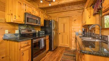 A wooden cabin kitchen with a stove, oven, microwave, refrigerator, and granite countertops.