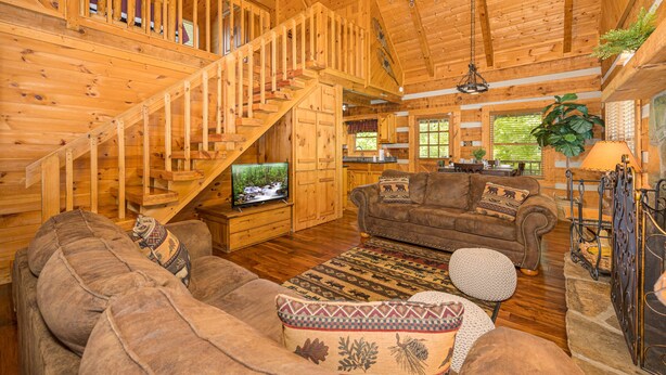 A wooden interior with a staircase, a television, a brown sofa, and a patterned rug. - Cozy2 BD Easily Accessible Cabin! Quiet community short drive to all attractions (Pigeon Forge)