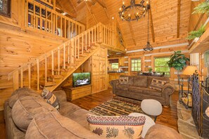 Un intérieur en bois avec un escalier, un téléviseur, un canapé marron et un tapis à motifs.