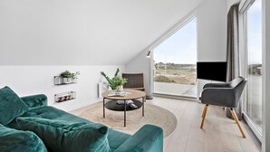 A modern living room with a green sofa, a round coffee table, and a view of the outdoors through large windows.