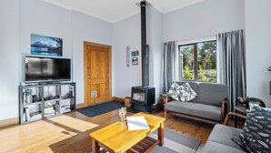 A modern living room with a TV, wooden furniture, a fireplace, and a large window. - Ekhaya - New Plymouth Holiday Home (New Plymouth)