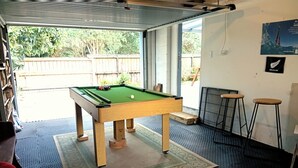 A pool table in a room with a patterned rug, a bar area with stools, and a view of the outdoors. - Ekhaya - New Plymouth Holiday Home (New Plymouth)