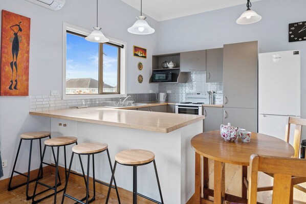 A modern kitchen with a central island, bar stools, a dining table, and a refrigerator.