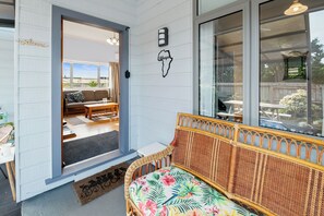 Un espacio de sala acogedor con un sofá de mimbre, una mesita y un banco. Una puerta da a un patio exterior con un sofá y una mesa.