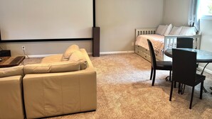 A room with a beige sofa, a small table, a bed with a white headboard, and a projector screen. - Recently Updated 3 Bedroom House, Fire Pit, Hot Tub, Game Room (New Buffalo)