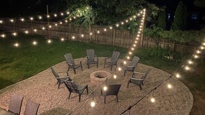 A circular outdoor seating area with a fire pit, surrounded by chairs and string lights. - Recently Updated 3 Bedroom House, Fire Pit, Hot Tub, Game Room (New Buffalo)