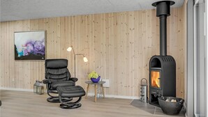 Una sala de estar moderna con un estufa de leña negra, un sillón de cuero negro, una pequeña mesa con un florero y un cuadro en la pared.
