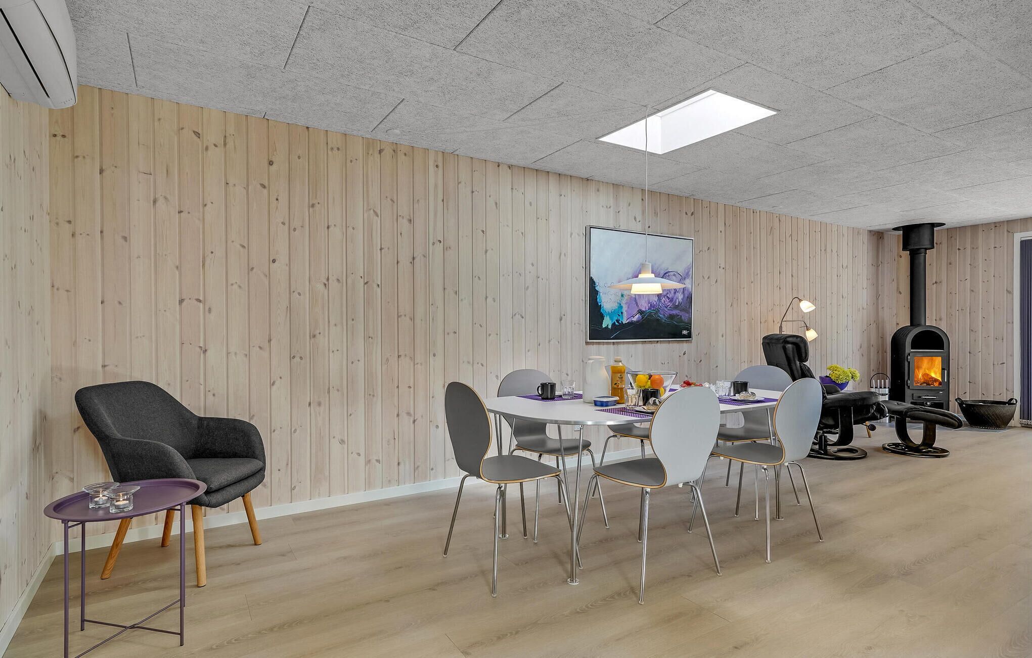 A modern dining area with a wooden wall, a painting, a fireplace, and a table with chairs.