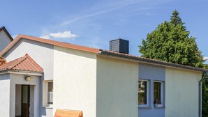 A single-story building with a red-tiled roof, a small porch with a bench, and a large tree in the background. - Nice home in Kalbe/ Milde -Kakerbec with WiFi (Kalbe/ Milde -Kakerbec)