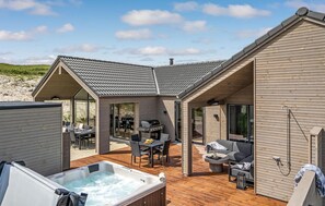 A modern outdoor living area with a hot tub, dining table, and seating. - Amazing home in Hvide Sande with sauna (Hvide Sande)