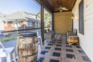 A covered outdoor patio with wicker furniture, two wooden barrels, and a ceiling fan.