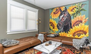 A living room with a brown leather sofa, a marble coffee table, and a large painting of a horse surrounded by sunflowers.