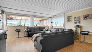 A modern living room with a sofa set, a desk, and a chair. There are large windows with curtains, a telescope, and framed photos on the wall. - 3 bedroom lovely home in Karrebæksminde (Karrebæksminde)