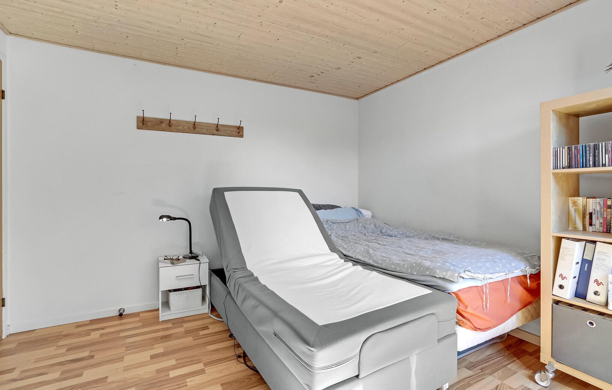 Une petite chambre à coucher, bien rangée, avec un lit, une table de chevet, une lampe et une bibliothèque.
