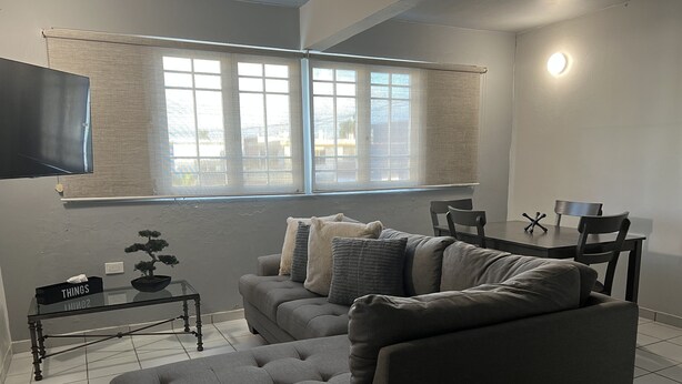A modern living room with a grey sofa, a small side table, and a TV mounted on the wall. - Private Apartment close to everything you need! (San Juan)