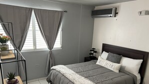 A bedroom with a bed, a nightstand, a potted plant, and a window with curtains. - Private Apartment close to everything you need! (San Juan)