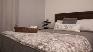 A neatly made bed with a patterned blanket, a bedside basket, a small bonsai tree, and a pillow with the text "SWEET DREAMS." - Private Apartment close to everything you need! (San Juan)