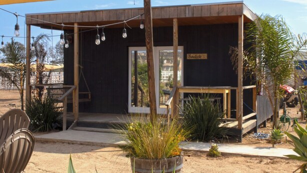 A small, dark-colored building with a wooden deck and a covered seating area. - VALLE LIFE (Valle de Guadalupe)