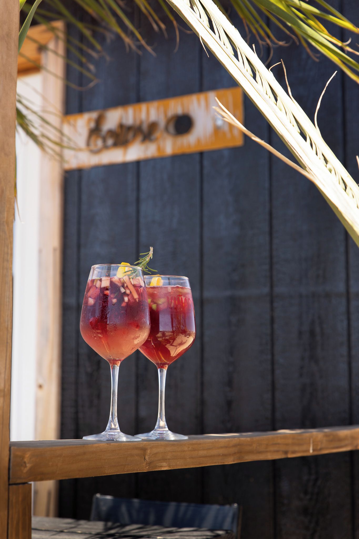 Dos vasos de bebida roja con decoración sobre una mesa de madera.