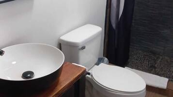 A bathroom with a wooden vanity, a white sink, a toilet, and a shower curtain.