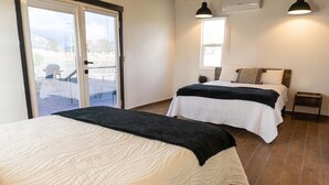 A bedroom with two beds, a sliding glass door to a balcony, and a view of the outdoors. - VALLE LIFE (Valle de Guadalupe)