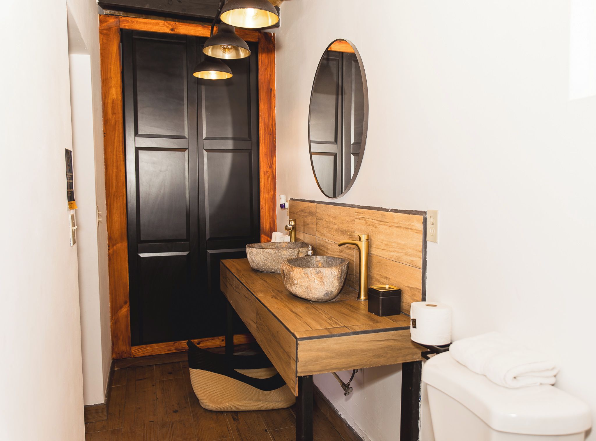 Un baño con tocador de madera, dos lavamanos de piedra, un inodoro, un espejo y una puerta con marco negro.