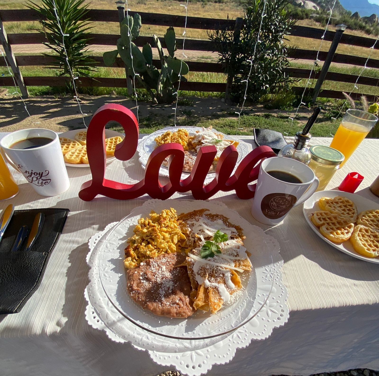 Un repas composé de gaufres, d’œufs brouillés et d’une boisson, servi sur une table à l’extérieur.