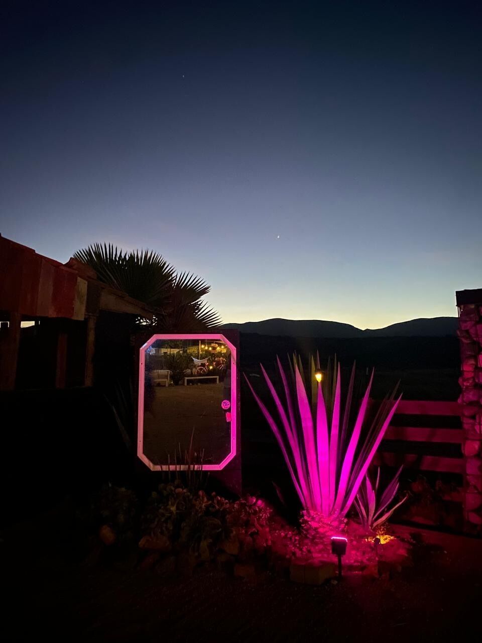 Une vue nocturne d’un paysage désertique, avec une structure illuminée en rose et une enseigne au néon.