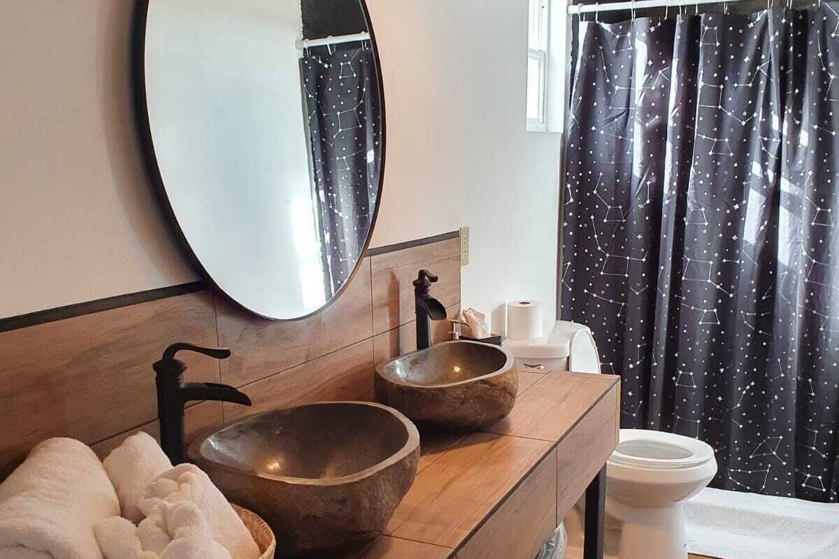 A modern bathroom with a wooden vanity, a round mirror, a freestanding sink, and a toilet.