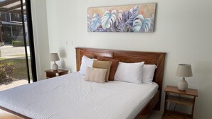 A large bed with a wooden headboard, white bedding, and multiple pillows. There are two bedside tables with lamps. A painting is on the wall above the bed.