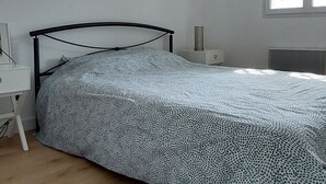 Une chambre à coucher comprenant un lit, une table de chevet, une lampe, une fenêtre et un luminaire au plafond.