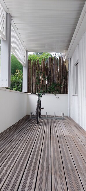 A covered outdoor area with a wooden floor, a bicycle, and a wooden fence with plants.