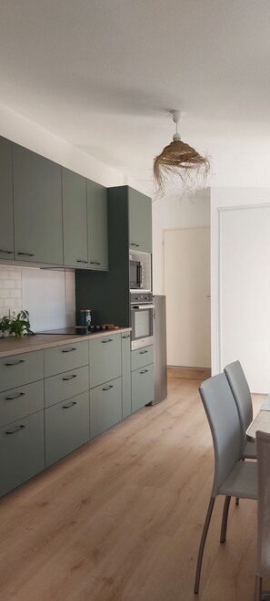 A modern kitchen with green cabinets, a built-in oven, and a dining area with a chair.