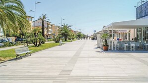 A wide pedestrian walkway lined with palm trees and benches, leading to a modern building with outdoor seating. - Cozy apartment in Lido di Camaiore with sauna (Lido di Camaiore)