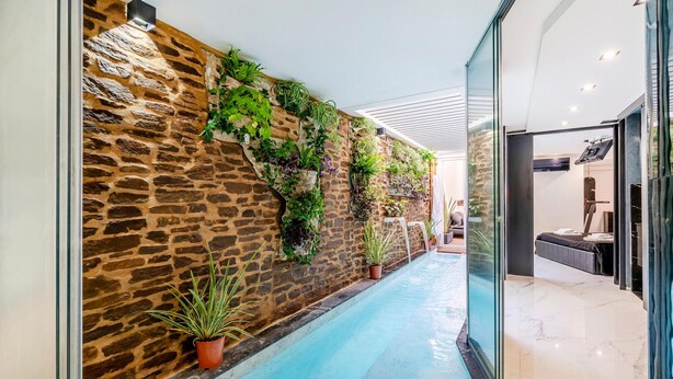 A corridor with a stone wall adorned with plants, a glass railing, and a pool. - Cozy apartment in Lido di Camaiore with sauna (Lido di Camaiore)
