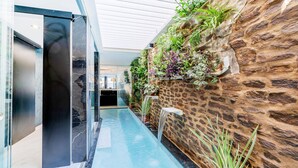 A modern hallway with a glass-enclosed pool, a stone wall with greenery, and a sleek black door. - Cozy apartment in Lido di Camaiore with sauna (Lido di Camaiore)