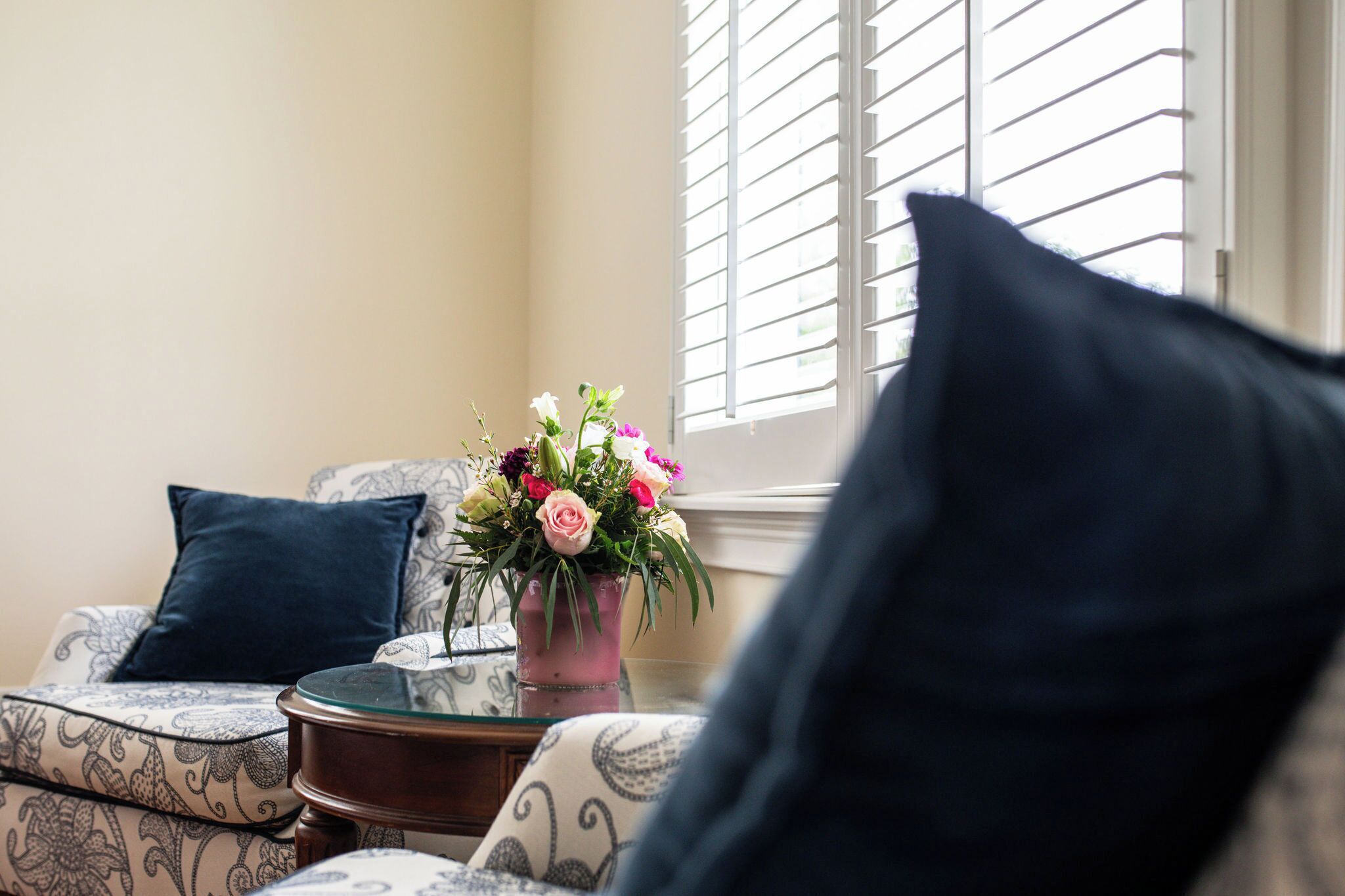 A living room with a sofa, a glass coffee table, and a vase with flowers.
