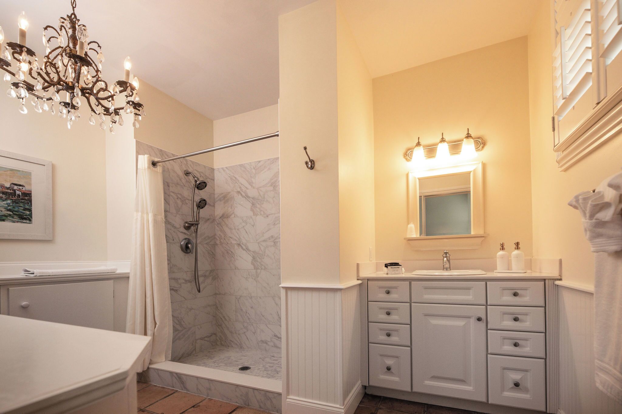 A bathroom with a shower, vanity, and a chandelier.