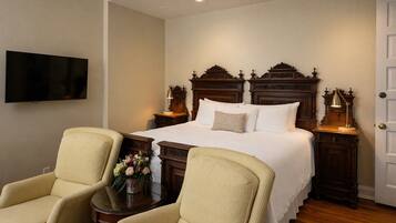 Una habitación de hotel con una cama grande, dos mesitas de noche con lámparas, un televisor en la pared y dos sillones tapizados.
