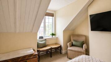 A cozy attic bedroom with a sloped ceiling, a window with a view, a chair, a bench, and a bed.