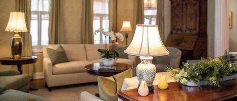 Een goed verlichte woonkamer met een bank, twee lampen, een houten kast en een tafel met decoratieve objecten.
