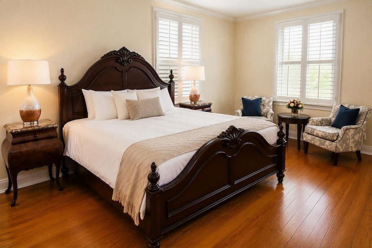 A bedroom with a large bed, two nightstands, a chair, and a window with blinds.
