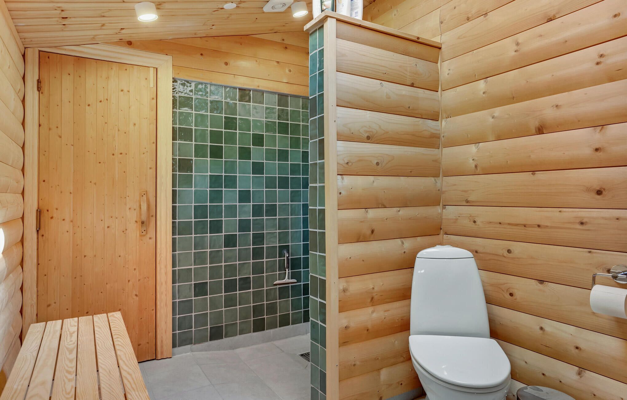 A wooden cabin bathroom with a toilet, a shower, and a bench.
