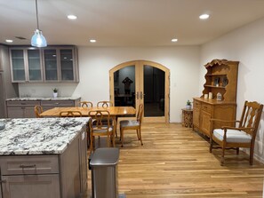 A dining area with a wooden table and chairs, a kitchen with cabinets, and a wooden cabinet with decorative items.