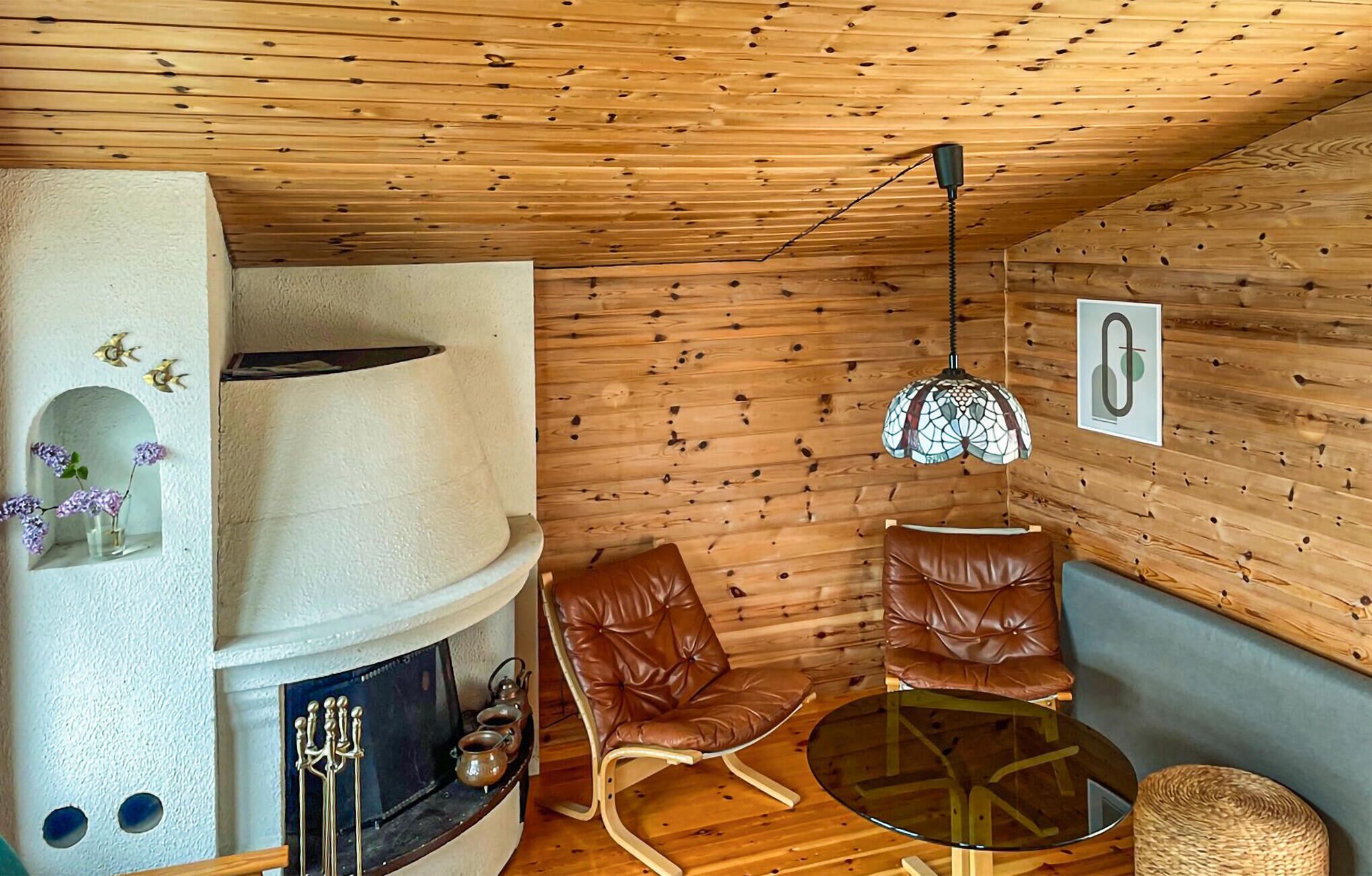 A cozy room with a wooden ceiling, a fireplace, leather chairs, a glass table, and a hanging light fixture.