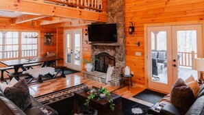 Ein gemütliches Blockhaus-Interieur mit Kamin aus Stein, Ledersofa und Essbereich.