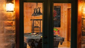 Eine Holztür mit Fensterglas, ein Billardtisch und eine Dartscheibe in einem Raum mit Backsteinwänden und Holzboden.